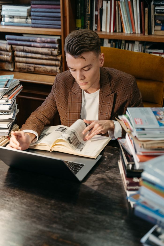 A young man studying diligently with books and a laptop in a library setting.